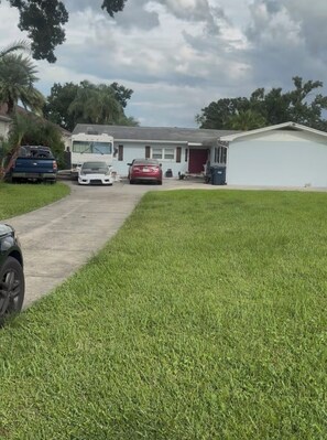 A residential driveway with a white car parked on the side, a red car in the driveway, and a blue truck parked on the left.