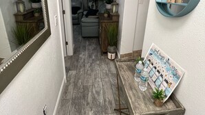 A hallway with a mirror, a small table with water bottles, and a decorative sign. - Tampa River Oasis (Tampa)