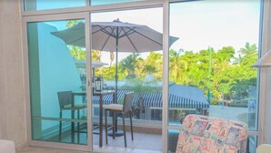 A room with a glass door leading to an outdoor area with a table and chairs, an umbrella, and a patterned chair. - Stylish Duplex Retreat 2BR Pool Nuevo Vallarta (Nuevo Vallarta)