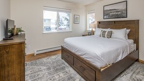 Un dormitorio con cama, cabecera de madera, mesitas de noche, ventilador de techo, ventana y alfombra.