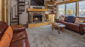A cozy living room with a fireplace, a leather sofa, a wooden coffee table, and a staircase leading to an upper level. - Big Sky Town Center condo w/fireplace & community pool/hot tub/sauna - The Grateful Getaway (Big Sky)