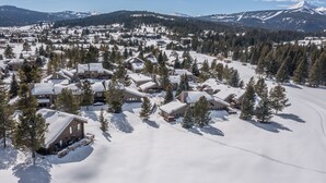 A snow-covered lodge with multiple cabins, surrounded by trees and mountains in the background. - Big Sky Town Center condo w/fireplace & community pool/hot tub/sauna - The Grateful Getaway (Big Sky)