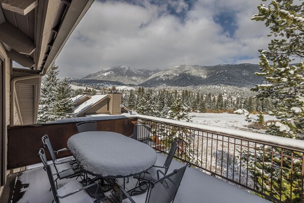 A balcony with a snow-covered table and chairs, overlooking a snowy mountain landscape.