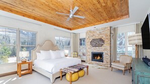 A spacious bedroom with a large bed, a wooden ceiling fan, a stone fireplace, and a view of the outdoors. - CASSIDY'S HIDEOUT- Beautiful Condo with Amazing San Sophia Ridge Views (Mountain Village)