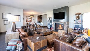 A spacious living room with leather sofas, a fireplace, a flat-screen TV, and a bookshelf. - CASSIDY'S HIDEOUT- Beautiful Condo with Amazing San Sophia Ridge Views (Mountain Village)