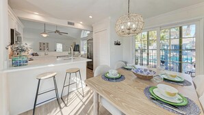 A modern kitchen with a central island, bar stools, and a dining area with a wooden table set for four. - Osprey in Blue Lagoon Unit 6 - Condo with Pool - By Island Real Estate Vacations (Holmes Beach)