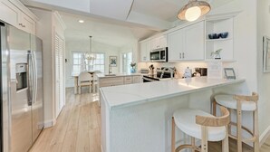 A modern kitchen with white cabinetry, a large island, and bar stools. - Osprey in Blue Lagoon Unit 6 - Condo with Pool - By Island Real Estate Vacations (Holmes Beach)