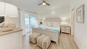 A bedroom with a bed, bedside tables, a lamp, a ceiling fan, and a window with curtains. - Osprey in Blue Lagoon Unit 6 - Condo with Pool - By Island Real Estate Vacations (Holmes Beach)