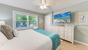 Ein Schlafzimmer mit einem großen Bett, einem Deckenventilator, einem an der Wand montierten Fernseher und einem Fenster mit Jalousien.