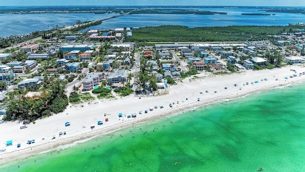 Luftaufnahme einer Küstenstadt mit Strand, Häusern und einem Yachthafen.