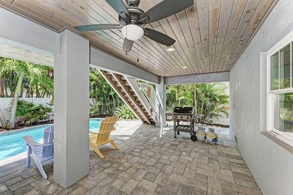 A covered patio with a ceiling fan, a pool, outdoor seating, and a barbecue area.