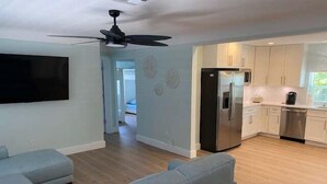 A modern living room with a flat-screen TV, a ceiling fan, and a light blue sofa. - Beach Life by the Gulf- Charming & Fully Equipped! (Redington Beach)
