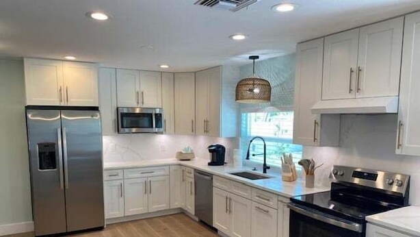 A modern kitchen with stainless steel appliances, white cabinetry, and a wooden floor. - Beach Life by the Gulf- Charming & Fully Equipped! (Redington Beach)