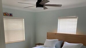 A bedroom with a wooden bed, white bedding, two bedside tables, and a ceiling fan. - Beach Life by the Gulf- Charming & Fully Equipped! (Redington Beach)