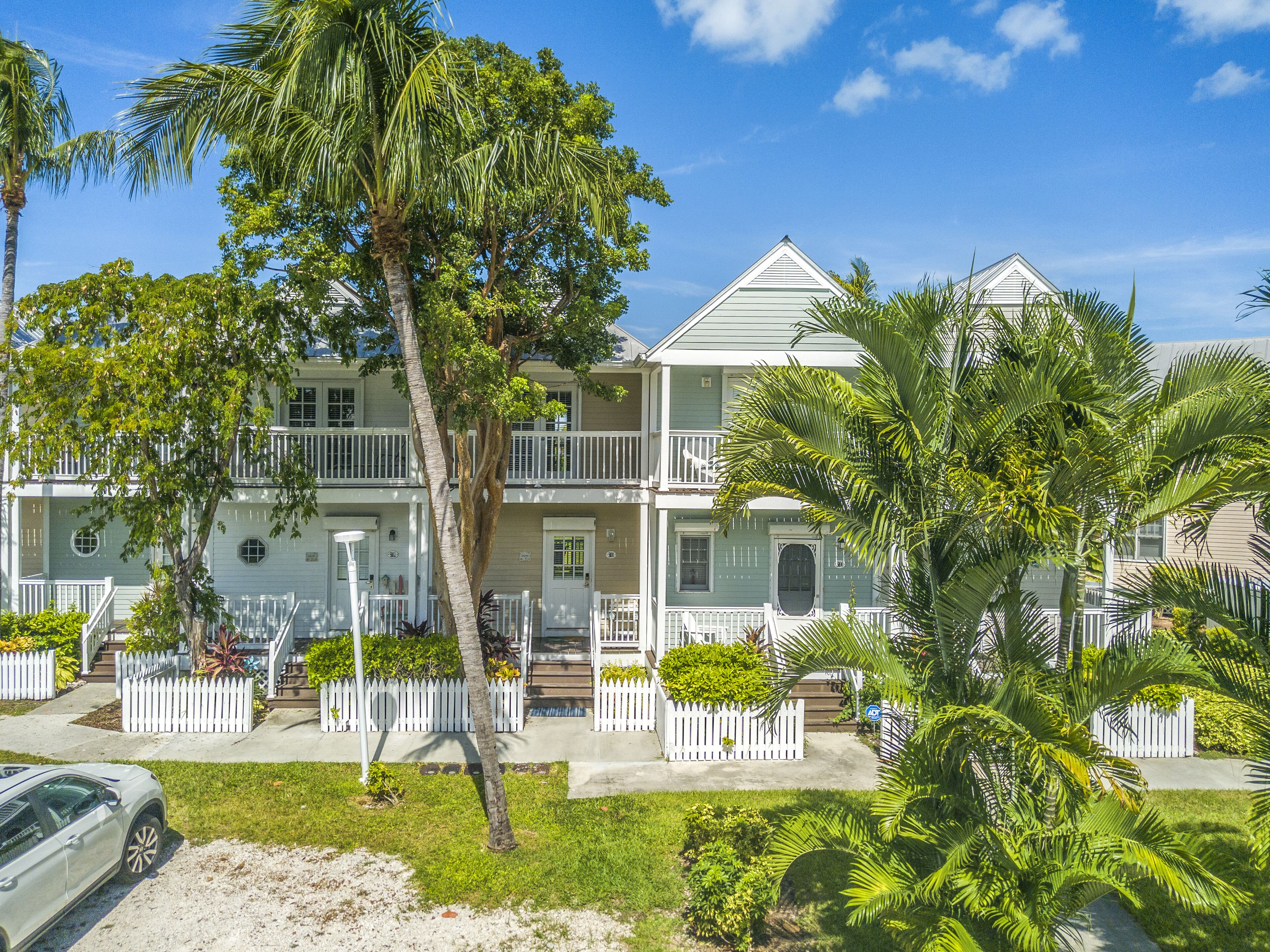 A two-story building with a white exterior, multiple balconies, and a white picket fence.