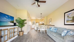 A spacious living area with a light blue sofa, a dining table with chairs, a large flat-screen TV, and a ceiling fan. - Waterfront Duck Key Villa - Sleeps 6 (Duck Key)