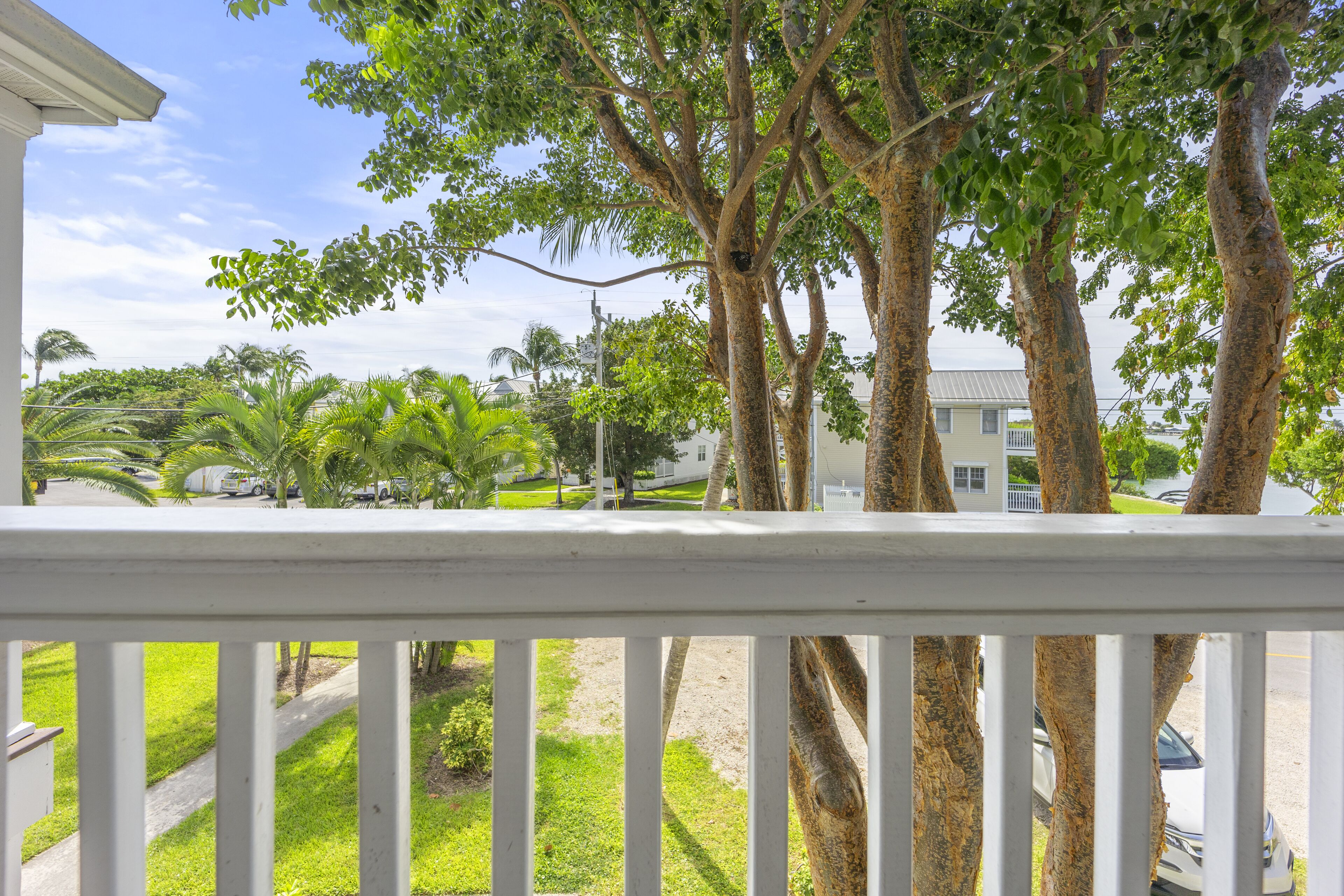 Vue depuis un balcon doté d’une balustrade, donnant sur un quartier résidentiel avec des arbres, une pelouse et une maison en arrière-plan.