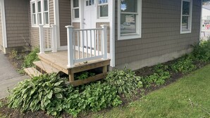 Una casa residencial con porche delantero, buzón y jardín con diversas plantas.