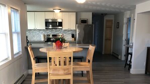 Una cocina moderna con armarios blancos, electrodomésticos de acero inoxidable y una mesa de madera con cuatro sillas.