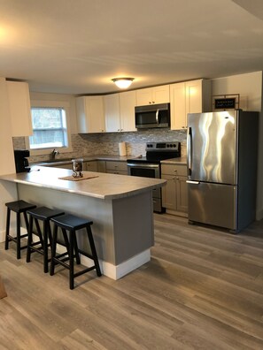 A modern kitchen with a central island, stainless steel appliances, and light wood flooring.