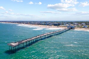 A pier extending into the ocean with a beach and residential area in the background.