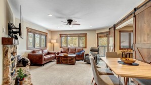 A spacious living room with a fireplace, leather sofas, a dining table with chairs, and large windows. - Relax in Breckenridge! Condo convenient to Skiing! Close to Downtown! (Breckenridge)