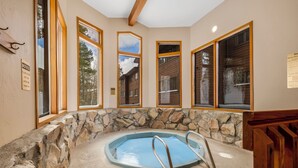A stone-walled hot tub with metal ladders, large windows with wooden frames, and a ceiling with exposed beams. - Relax in Breckenridge! Condo convenient to Skiing! Close to Downtown! (Breckenridge)