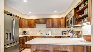A modern kitchen with wooden cabinets, stainless steel appliances, and a large island with stools. - Relax in Breckenridge! Condo convenient to Skiing! Close to Downtown! (Breckenridge)