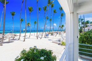 A beach view with palm trees, a sandy beach, and a clear blue sky. - Affordable Luxury Oceanfront 3BR Apartment in Bávaro Beach (Punta Cana)