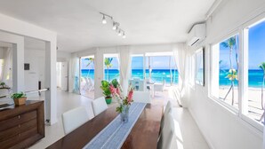 A spacious room with a large wooden dining table, white chairs, and a view of the ocean through large windows. - Ocean View Luxury Apartment Directly on the Los Corales Beach (Punta Cana)