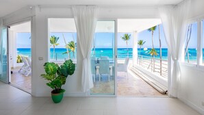 A spacious room with a large sliding glass door leading to a balcony with a view of the ocean and palm trees. - Ocean View Luxury Apartment Directly on the Los Corales Beach (Punta Cana)