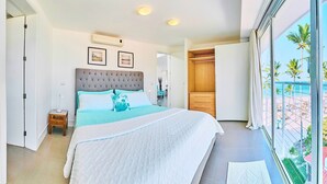 A modern bedroom with a large bed, a walk-in closet, and a balcony with a view of the beach. - Punta Cana Beachfront Penthouse - Ocean View, BBQ, Terrace, 4BR (Punta Cana)