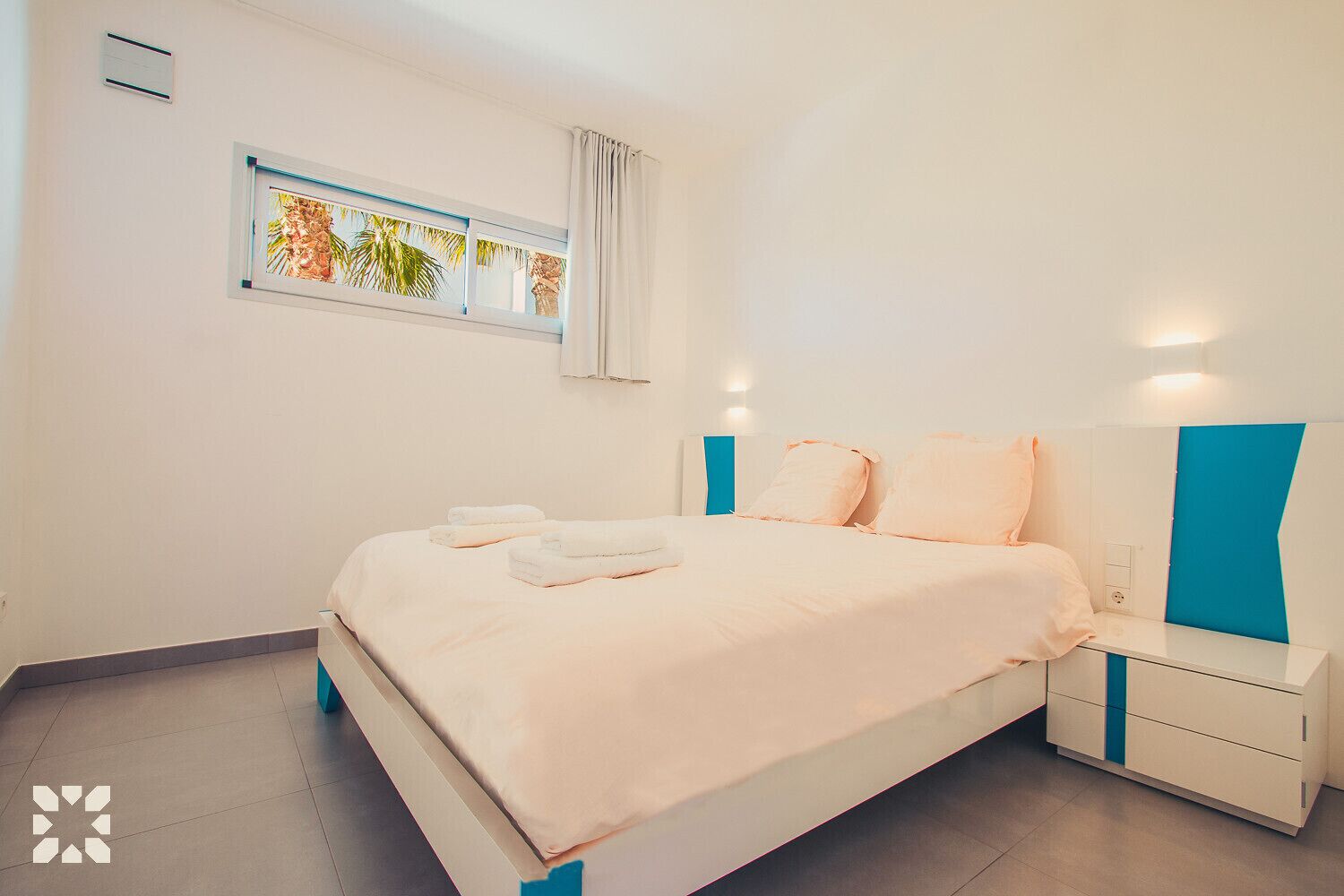 Een moderne slaapkamer met een bed, nachtkastjes en een raam met uitzicht op palmbomen.