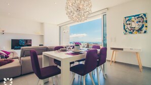 Un salon moderne comprenant un coin repas, une grande fenêtre offrant une vue dégagée, un lustre et un tableau accroché au mur.