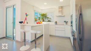Une cuisine moderne avec des meubles blancs, un réfrigérateur en acier inoxydable et un coin bar équipé de tabourets.