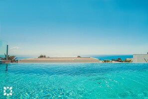 A clear blue pool with a view of the sea and a distant beach.