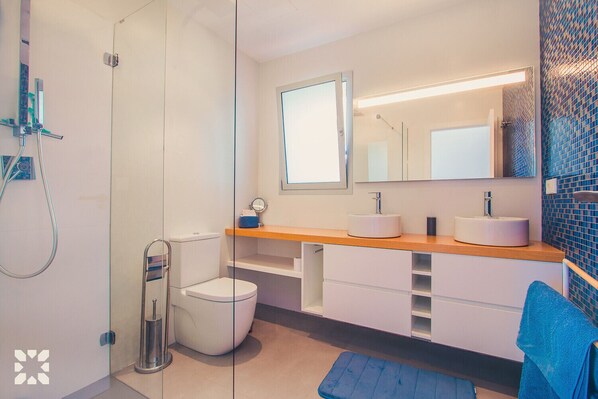 A modern bathroom with a glass shower enclosure, a toilet, a sink with a mirror above, and a blue towel on the floor.