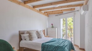 Une chambre avec un plafond en bois, un lit recouvert d’une couverture verte, une commode et une fenêtre donnant sur un paysage verdoyant.