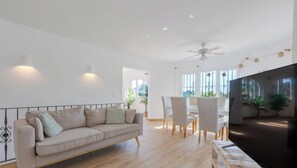 A modern living room with a sofa, dining table, chairs, and a flat-screen TV.