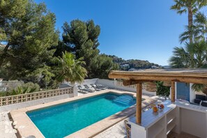 Une piscine dotée de chaises longues, d’une pergola et offrant une vue sur un paysage vallonné.