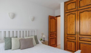 Une chambre à coucher avec un lit, des oreillers, une table de chevet avec une lampe et une armoire en bois.