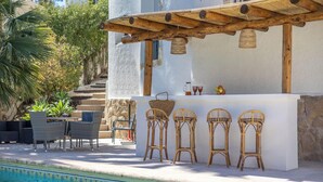 Un bar situé au bord de la piscine, avec des chaises en osier et un comptoir blanc.