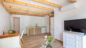 Un espace de vie moderne doté d’un plafond en bois, d’un téléviseur à écran plat, d’un coin repas avec une table et des chaises, et d’une kitchenette équipée d’un évier et de placards.