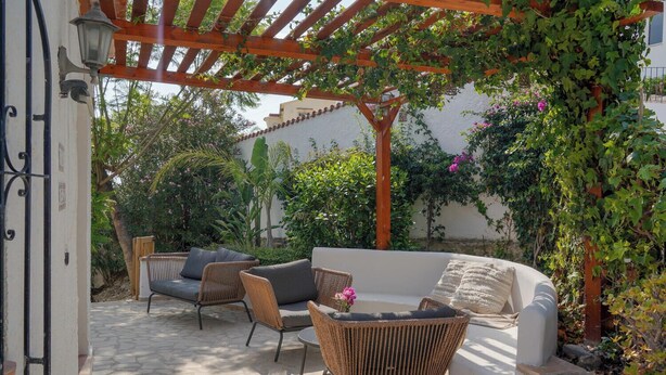 Un espace extérieur aménagé avec des meubles en osier et un canapé blanc, le tout installé sous une pergola en bois.