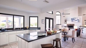 Una cocina moderna con armarios blancos, una isla central y un comedor con sillas.