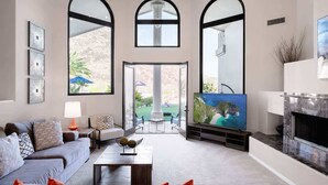 Amplia sala de estar con televisor grande, chimenea y vistas a un patio con mobiliario exterior.