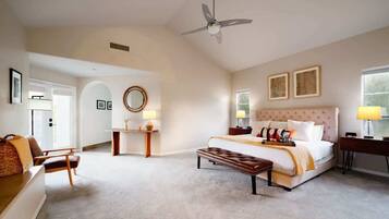 A spacious bedroom with a large bed, a sitting area with a chair, a desk, and a ceiling fan.