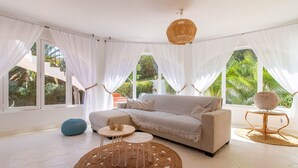 A spacious living room with a beige sofa, round coffee table, and a decorative lamp. Large windows with sheer curtains allow natural light to fill the room. - Villa CASA PIPA by Abahana Villas (Benissa)