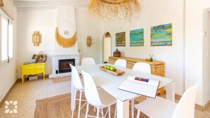 A dining area with a white table, white chairs, a yellow side table, a fireplace, and artwork on the wall. - Villa CASA PIPA by Abahana Villas (Benissa)