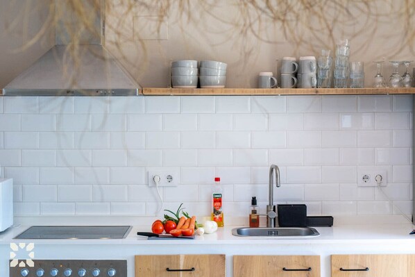 A modern kitchen with white tiles, a stainless steel sink, and wooden cabinets.